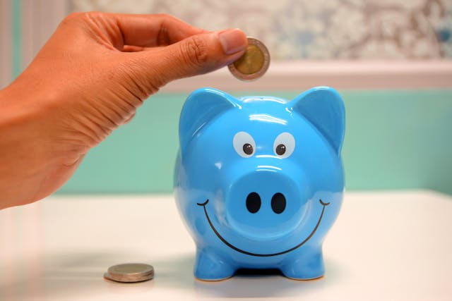 someone putting coins in a blue piggy bank